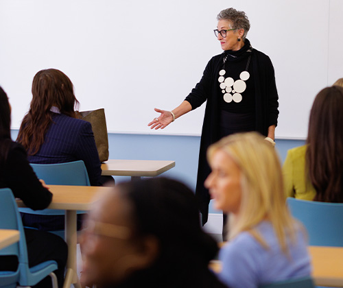 A classroom with students sitting facing a professor at the front who is standing and talking